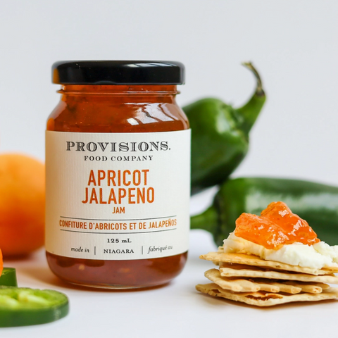 Jar of Provisions Apricot Jalapeno jam with apricots, jalapenos, and crackers on a white background