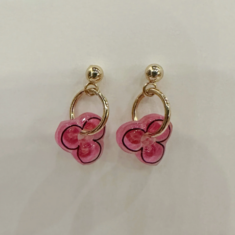 Pair of pink flower-shaped earrings with gold loops on a light beige background