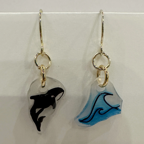 Pair of earrings with whale designs on clear stones against a white background