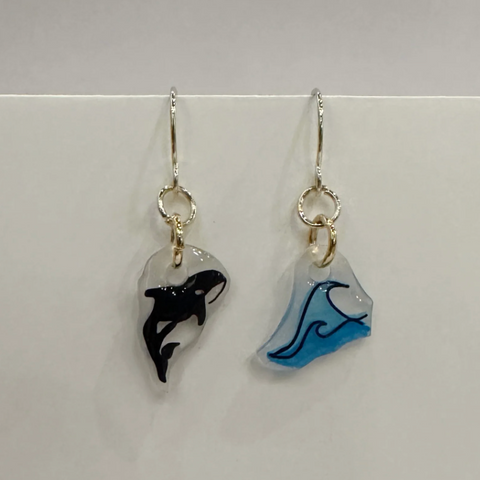 Pair of earrings with whale and wave designs on a white background