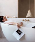 Woman relaxing in a bathtub with a book, surrounded by minimal decor.