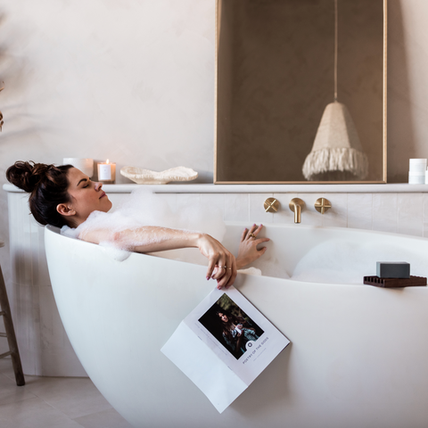Woman relaxing in a bathtub with a book, surrounded by minimal decor.