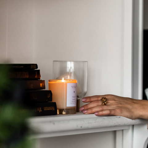Hand holding a lit candle next to a Christmas tree with blurred background