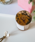 Jar with tortoiseshell lid on a light surface with scissors and plant in the background