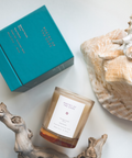 Candle with a label, teal box, and seashell on a light surface