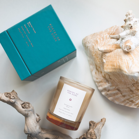 Candle with a label, teal box, and seashell on a light surface