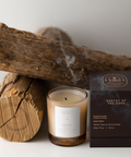 Candle with packaging and wooden logs on a white background