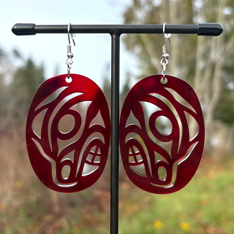 Red and silver tribal-style earrings on a stand with a blurred natural background