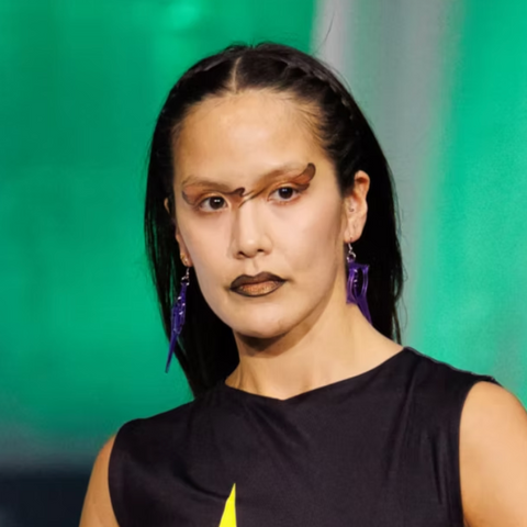 Woman wearing purple earrings against a green background