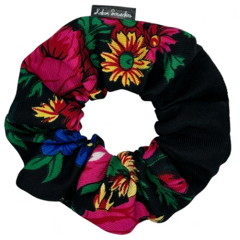 Colorful floral scrunchie on a black background with a brand tag.