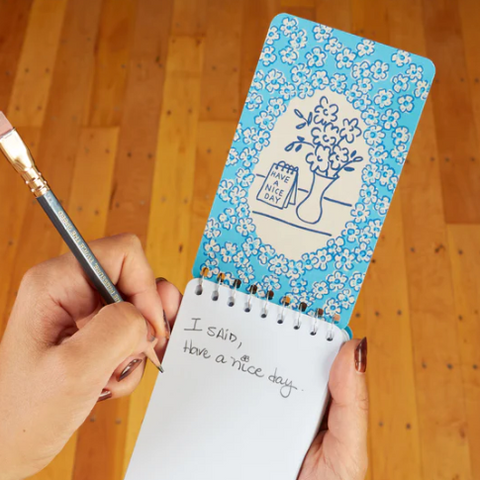 Notebook with floral design held by a hand on a wooden surface, with product details on the right.