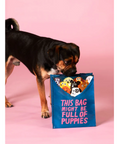 Dog holding a blue tote bag with cartoon puppies on a pink background
