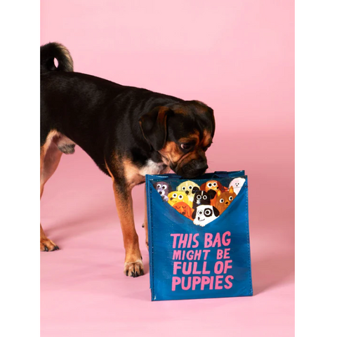 Dog holding a blue tote bag with cartoon puppies on a pink background