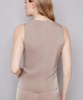 Woman wearing a beige sleeveless top and pants against a gray background