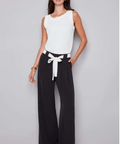 Woman wearing a white sleeveless top and black wide-leg pants with a white belt against a gray background
