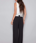 Woman wearing a white top and black wide-leg pants against a gray background