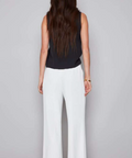 Woman wearing a black sleeveless top and white pants on a gray background