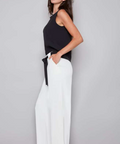 Woman wearing a black top and white pants against a gray background