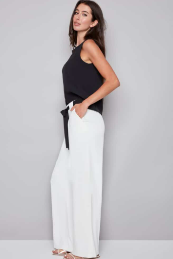 Woman wearing a black top and white pants against a gray background