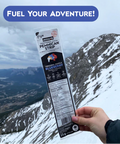 Hand holding a package of Mitsinjo berries with a mountainous landscape in the background and 'Fuel Your Adventure!' text.