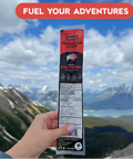 Hand holding a package of Pemmican Strip with mountains in the background
