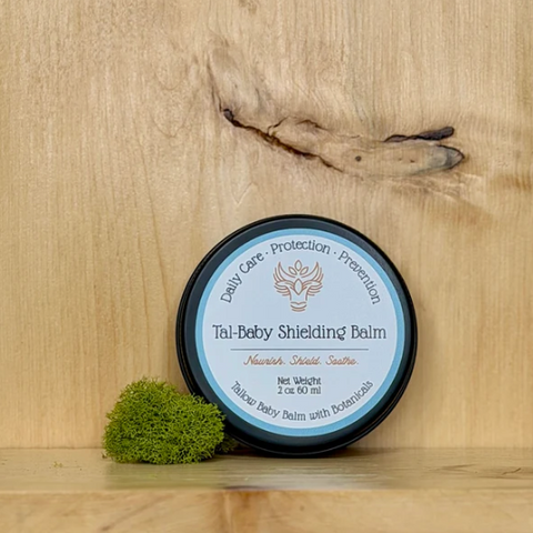 Tal-Baby Shielding Balm on a wooden surface with a small green plant.