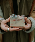 Person holding a bar of soap with a natural pattern, wearing a brown coat.