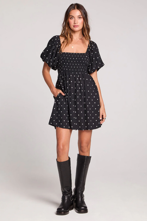 Woman wearing a black dress with white polka dots and black boots on a white background
