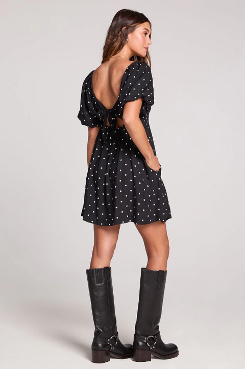 Woman wearing a black dress with white polka dots and black boots on a white background