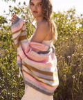Woman wearing a colorful striped sweater over a white dress in a natural setting