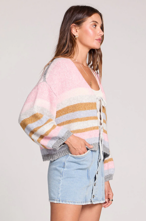 Woman wearing a colorful striped sweater and denim shorts on a plain background