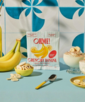 Packaging of OHME! Crunchy Banana with bananas, nuts, and dessert on a blue surface with a tiled wall background.