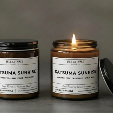 Two candles labeled 'Satsuma Sunrise' on a gray surface with a blurred background