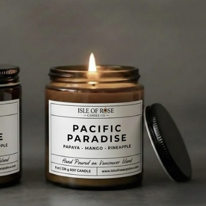 Two candles labeled 'Pacific Paradise' by Isle of Rose on a dark surface.
