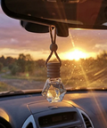 Car dashboard with a hanging car air freshener against a scenic sunset background