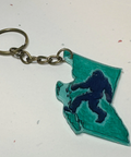 Keychain shaped like the outline of British Columbia with a silhouette of a Sasquatch, on a plain background.