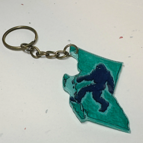 Keychain shaped like the outline of British Columbia with a silhouette of a Sasquatch, on a plain background.