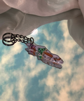 Keychain with cartoon design held by a hand against a cloudy sky background