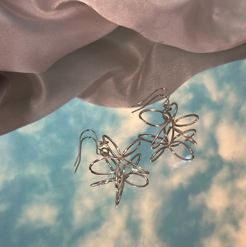 Silver floral earrings on a soft fabric background