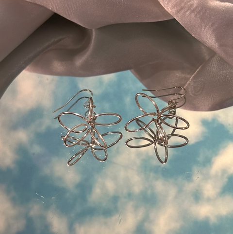 Silver wire flower earrings on a soft fabric background