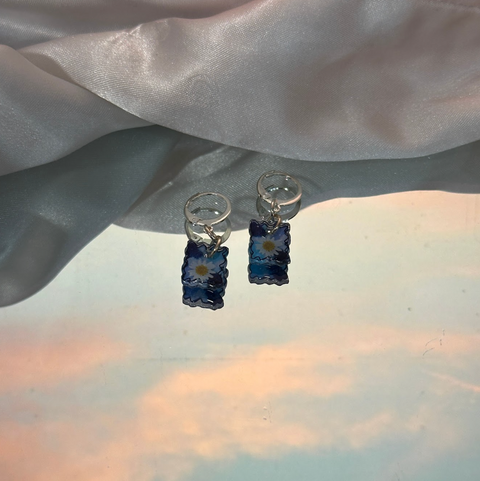 Pair of earrings with blue floral design on a light fabric background