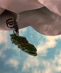 Keychain with a green leaf design against a cloudy sky