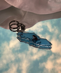 Keychain with a whale design held against a cloudy sky