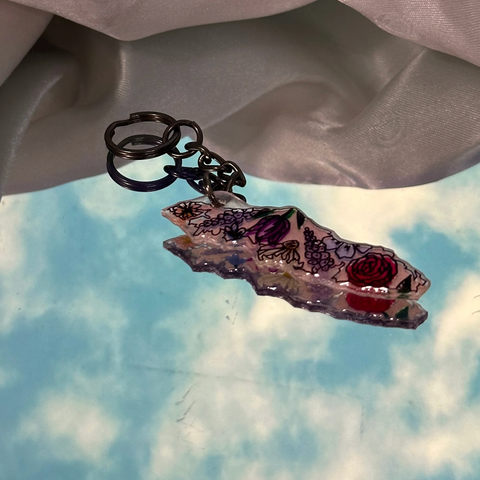 Decorative keychain with floral design against a cloudy sky background