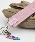 Pink keychain strap with a bottle opener and charm on a wooden surface