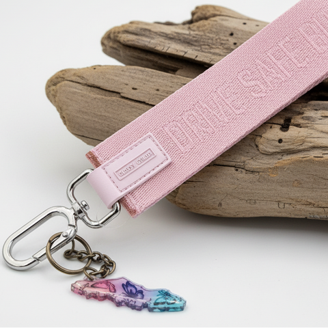 Pink keychain strap with a bottle opener and charm on a wooden surface