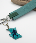 Keychain with teal ribbon, keyring, and Bigfoot silhouette on a wooden surface