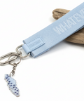 Light blue keychain with 'WHATEVER' text on a wooden surface