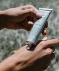 Hand holding a tube of skincare product against a natural background