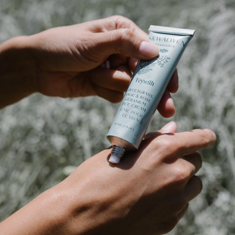 Hand holding a tube of skincare product against a natural background